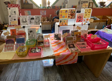An array of products displayed on a location-provided table, about 6 ft. in length. This shot is of the whole table.
